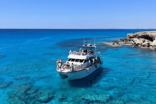 Tour boat with passengers anchored in the clear blue water off the Cape Greco coastline near Ayia Napa