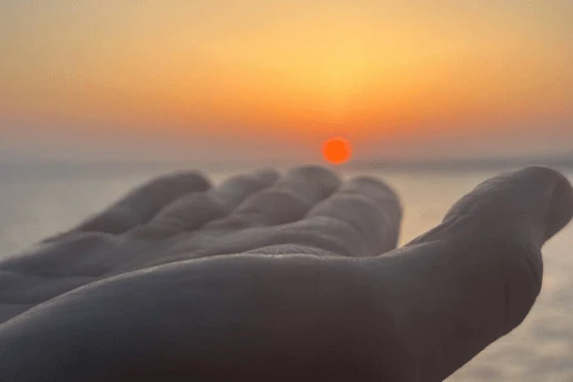 Hand reaching toward the setting sun over the sea on a Cyprus sunset cruise