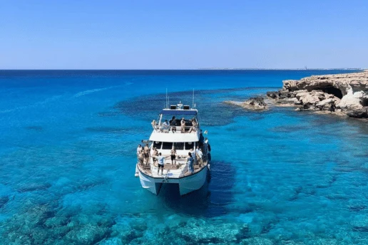 Catamaran with passengers anchored in clear turquoise water by the Cape Greco coastline