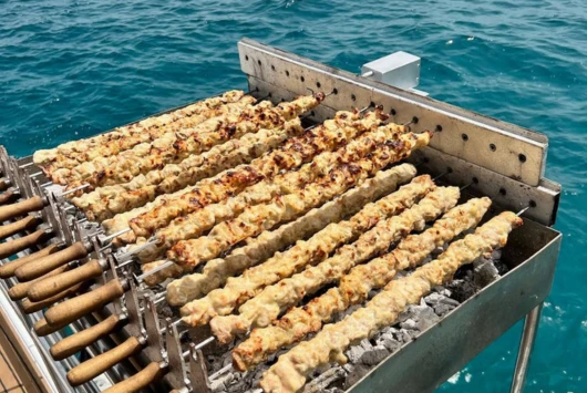 Chicken souvlaki grilling on the BBQ over the sea on a SCUBACAT cruise