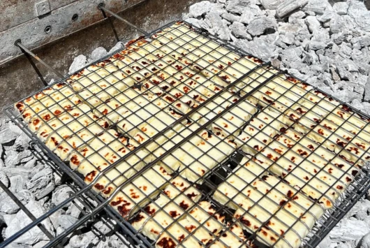 Slices of Cypriot halloumi grilling on the charcoal BBQ on board