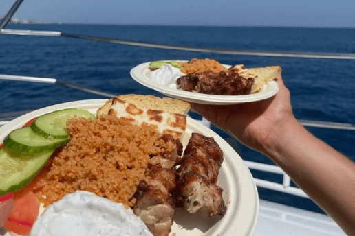 Two plates of BBQ chicken, halloumi, pourgouri and salad served on deck at sea