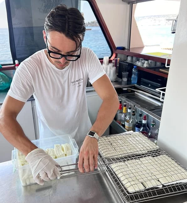 SCUBACAT crew member preparing halloumi in the galley on board the catamaran