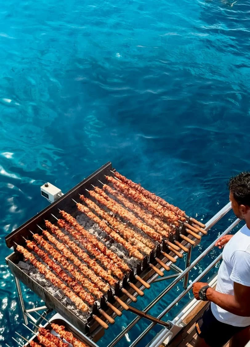 Crew member grilling skewers of chicken souvlaki on the back deck of the catamaran
