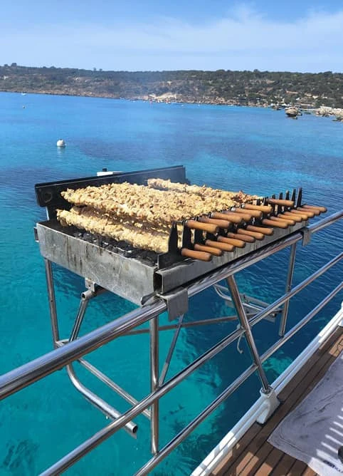 Charcoal grill loaded with chicken souvlaki over the sea on the back deck