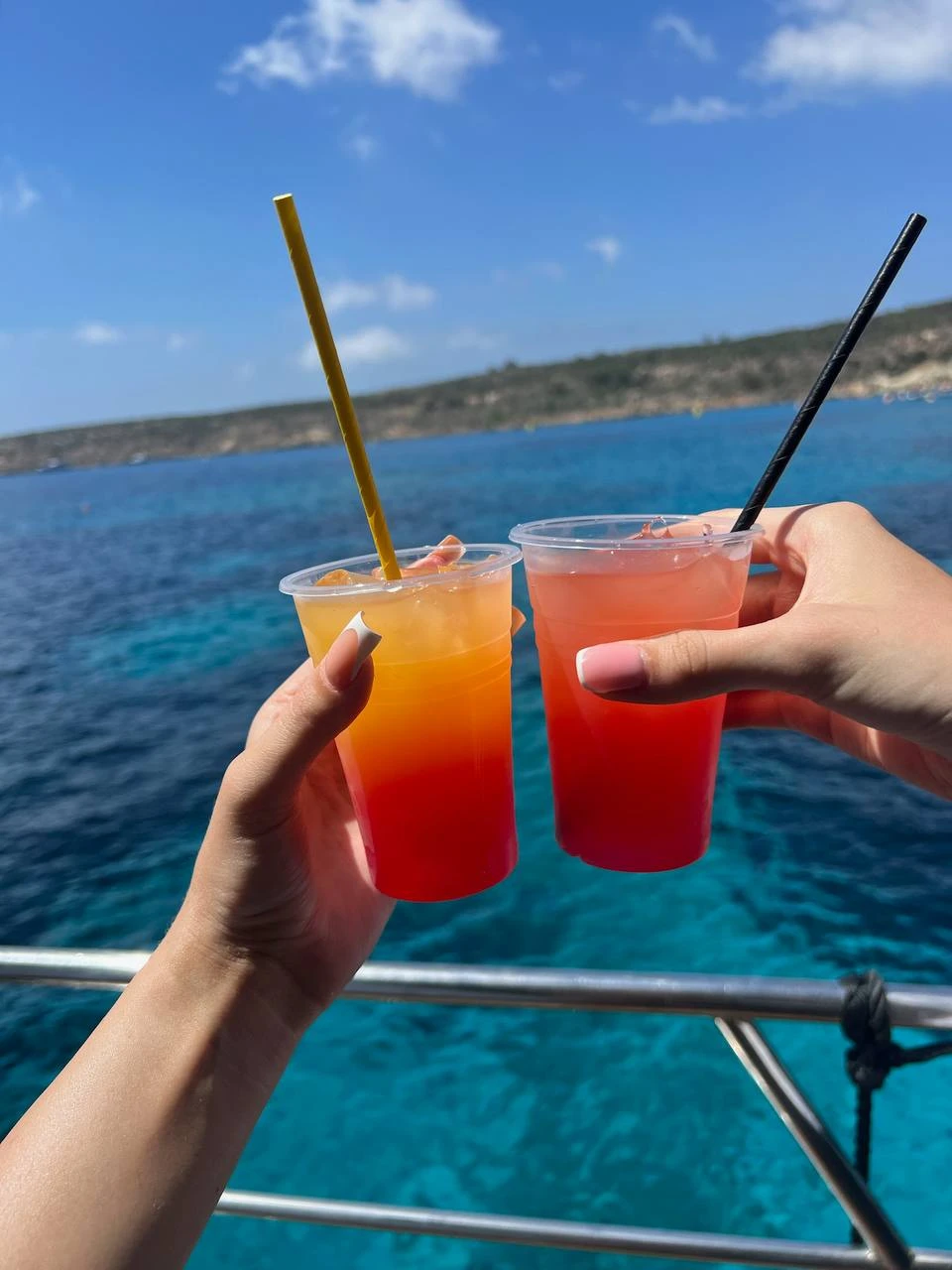 Two colourful drinks from the onboard bar held up over the sea