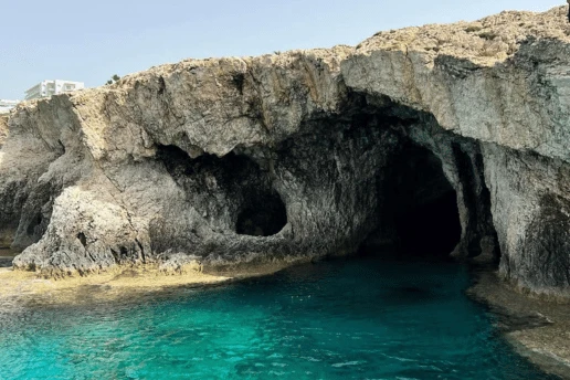 Rock arch and sea caves over shallow turquoise water, with a hotel building on the clifftop near Ayia Napa