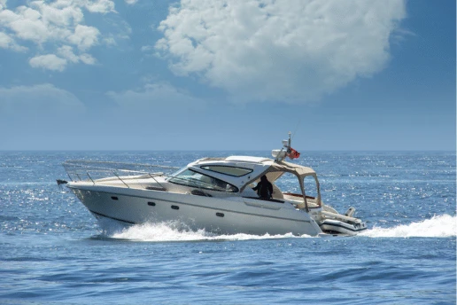 White motor cruiser speeding across open sea, with one person at the helm and a flag flying at the stern