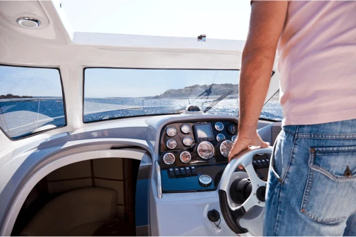Person steering a small motorboat at the helm, with gauges on the dashboard and a rocky coast ahead