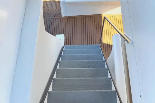 Metal stairs with a handrail leading down from the upper deck to the teak lower deck of a catamaran