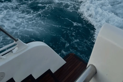 White wake behind a catamaran moving through deep blue water, seen from the stern steps
