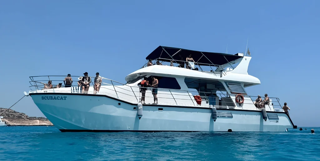 The Scubacat catamaran at anchor in turquoise water, with guests on both decks and swimmers at the stern