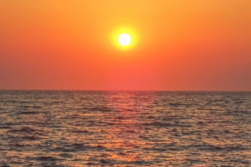 Sun low over a calm sea under an orange sky, with light reflecting on the water