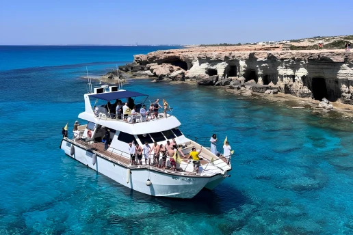 Double-deck catamaran with guests on board, stopped in turquoise water beside the sea caves near Cape Greco