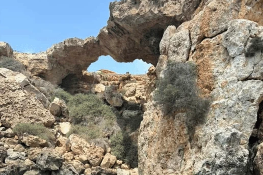 Natural rock arch above a rocky shore and clear turquoise water, seen from a boat close to the cliffs