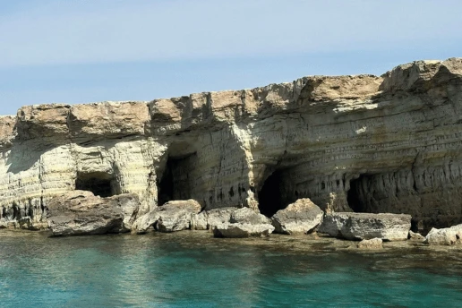 Layered limestone cliff with sea caves at water level above calm turquoise water near Cape Greco