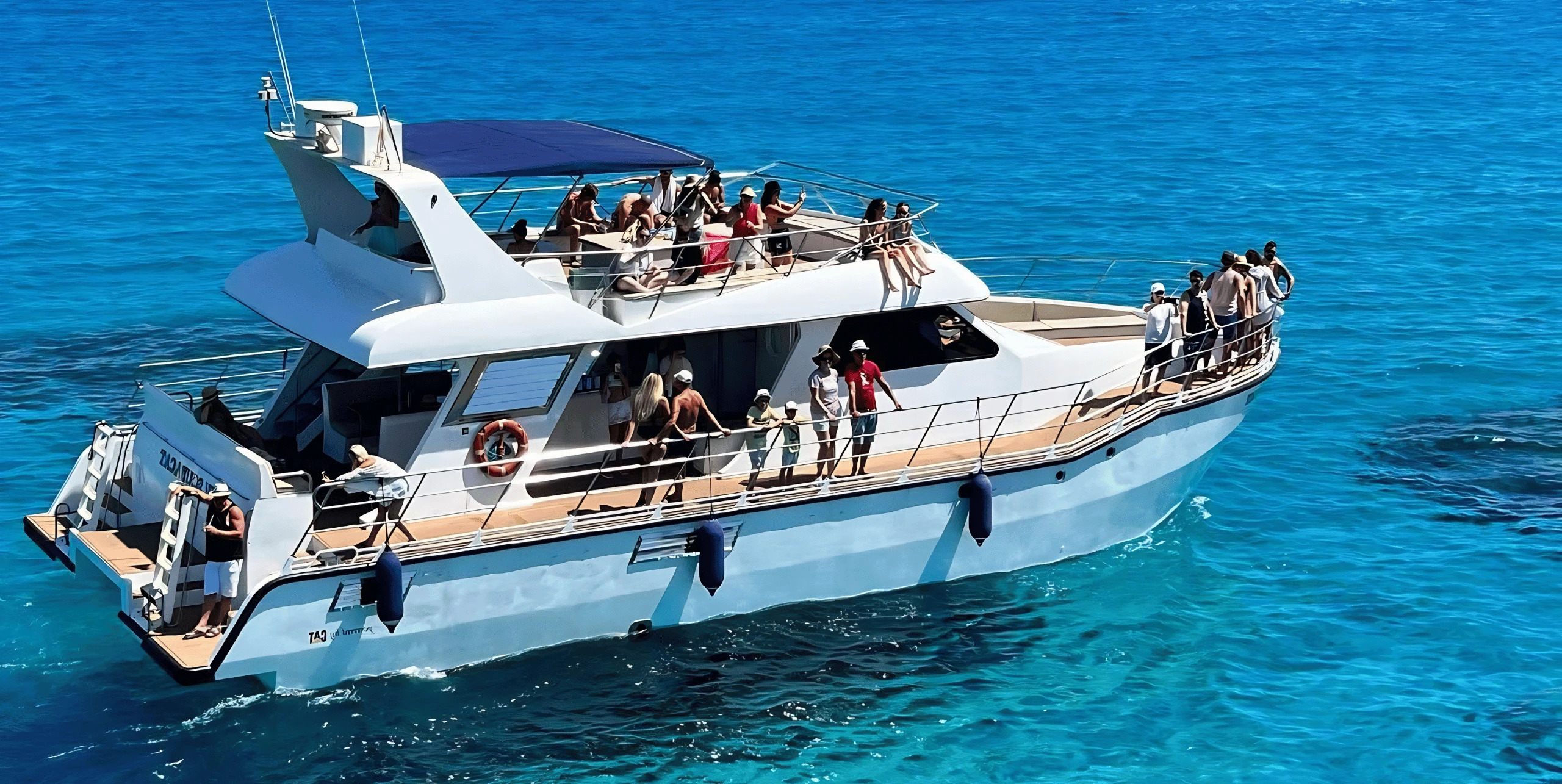 The Scubacat catamaran on turquoise water, with guests along the rails, on the upper deck and at the bow
