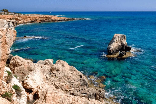 Rocky limestone coastline with a sea stack standing in clear turquoise water under a blue sky